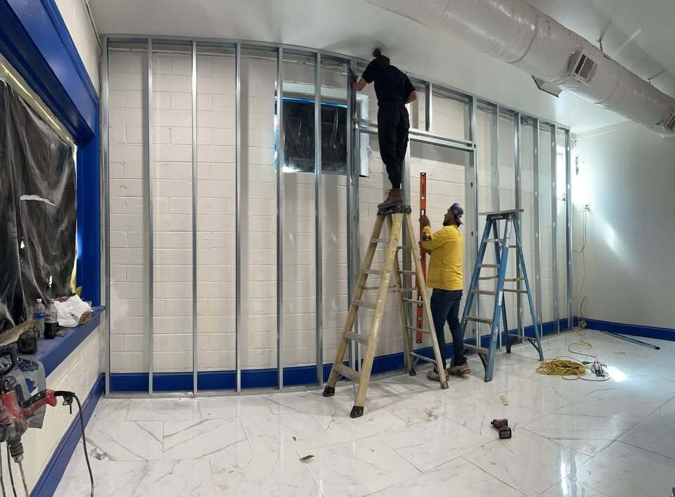 Two HR Builders workers installing metal stud framing along a commercial wall